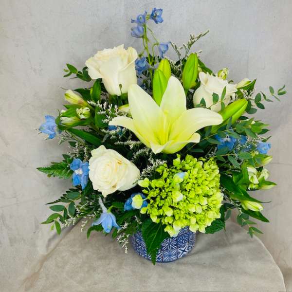 White lilies and roses with blue flowers in a patterned vase