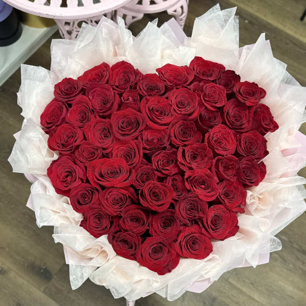 Heart-shaped bouquet of red roses wrapped in pale pink and white tissue paper