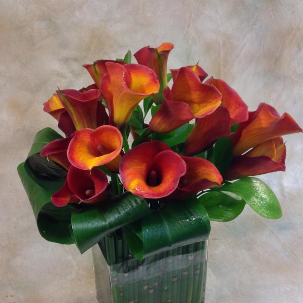 Arrangement of red and orange calla lilies in a square glass vase