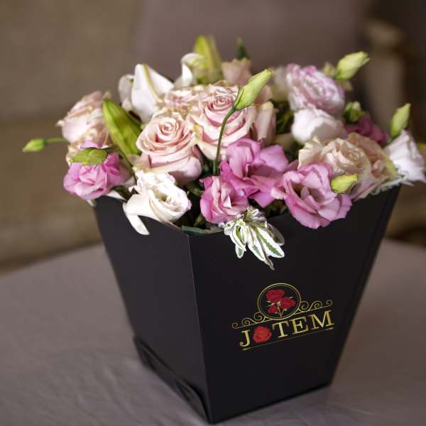 Pink and white roses in a black box with a gold logo
