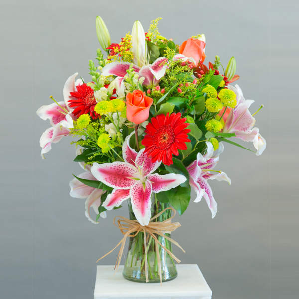 Mixed bouquet of lilies, roses, and gerbera daisies in a glass vase