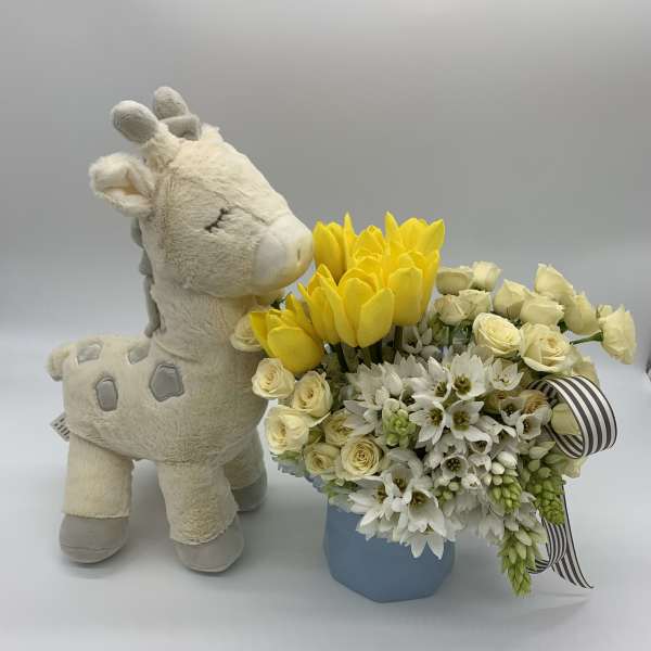 Plush giraffe beside a yellow and white flower arrangement in a blue box