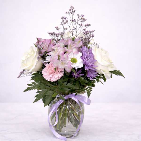 Pink and white mixed bouquet in a glass vase with a lavender ribbon
