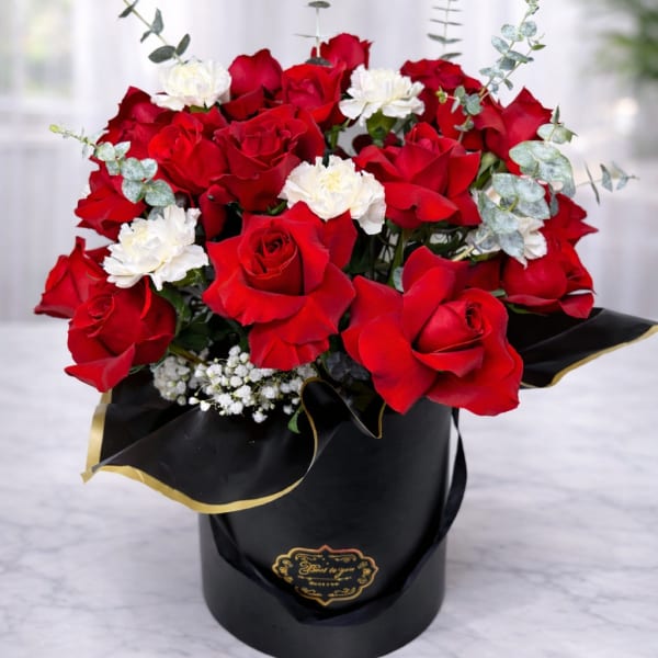 Red roses and white carnations arranged in a black hatbox