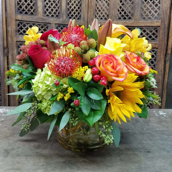 Mixed bouquet in a glass vase with roses, sunflowers, and orchids