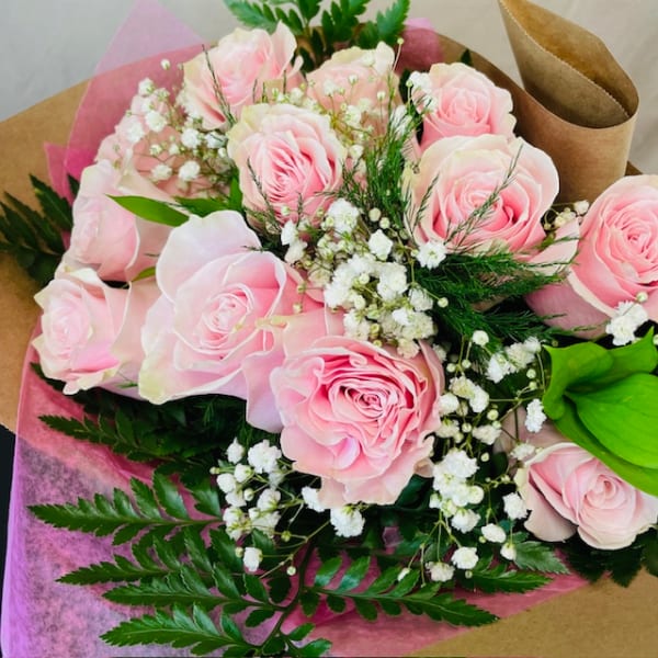 Bouquet of pale pink roses with baby's breath and greenery wrapped in pink and brown paper