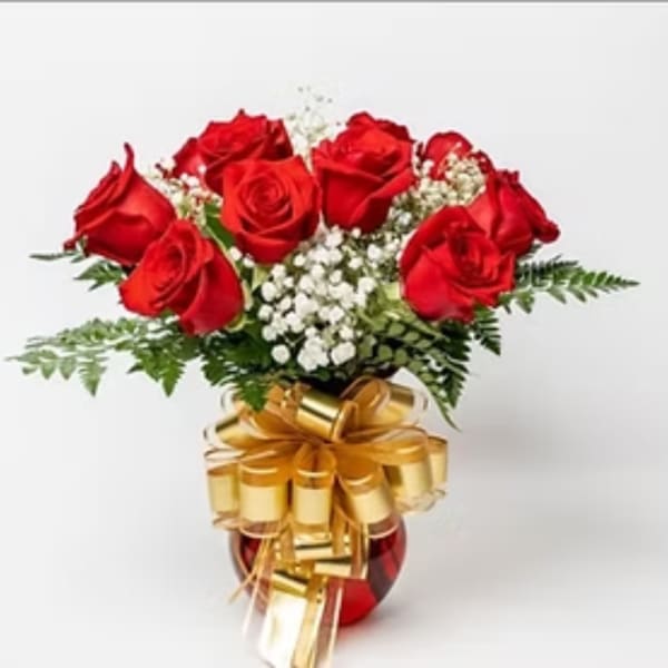 Red roses arranged in a vase with white filler flowers and a gold bow