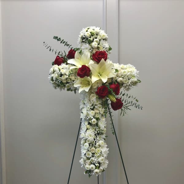 White floral cross arrangement with red roses on a stand