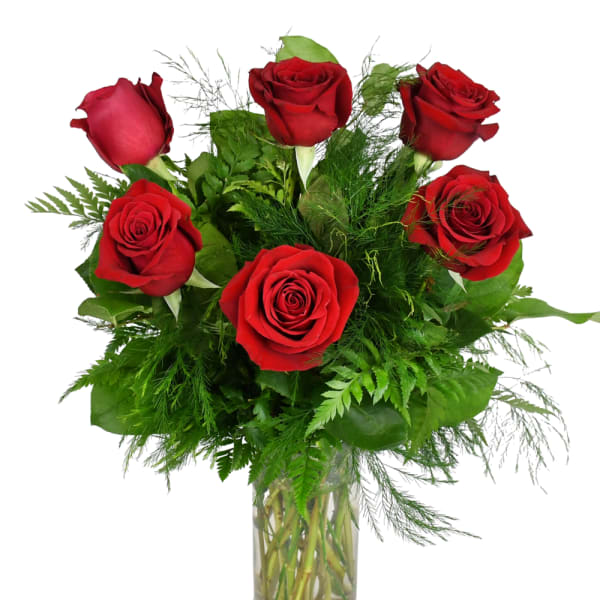 Red roses arranged in a clear glass vase with green foliage