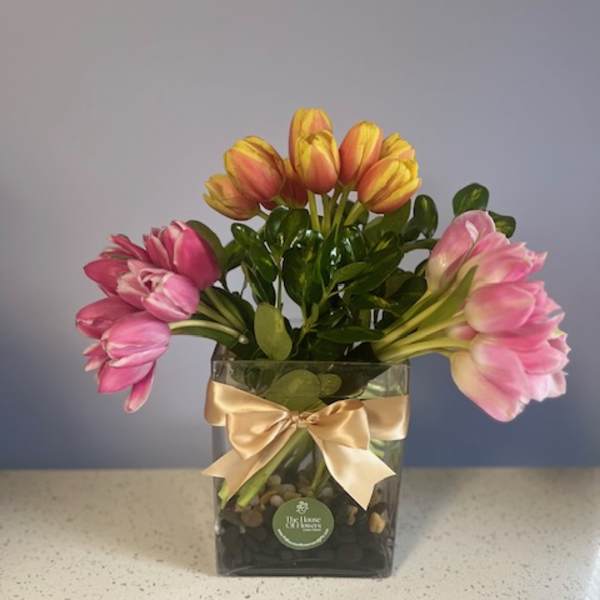 Pink and yellow tulips in a square glass vase with a gold ribbon