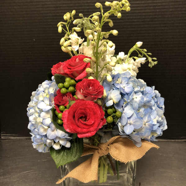 Bouquet of red roses and blue hydrangeas in a glass vase with a burlap bow