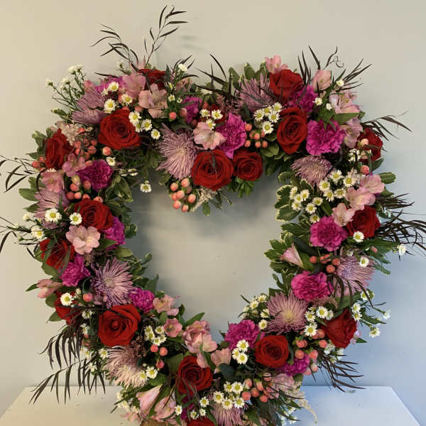Heart-shaped floral wreath with red roses and pink blooms on a wood base