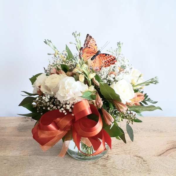 Mixed white and peach bouquet in a glass vase with a red ribbon and butterfly topper