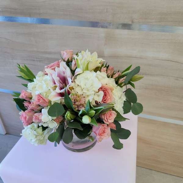 Low arrangement of pink roses, white hydrangeas, and lilies in a clear glass bowl vase