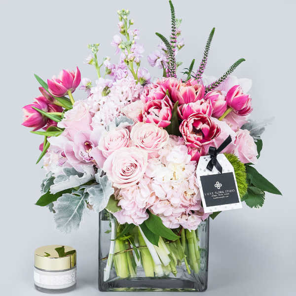 Pink tulips and roses arranged in a square glass vase with a candle beside it.