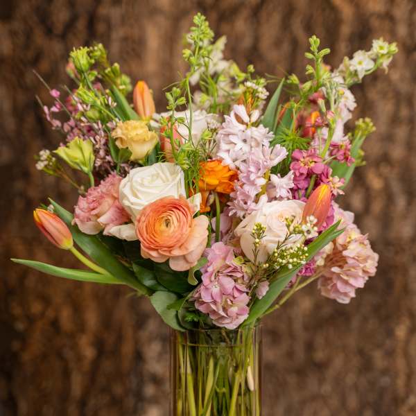 Tall mixed bouquet of pink, peach, and white flowers in a clear glass vase.