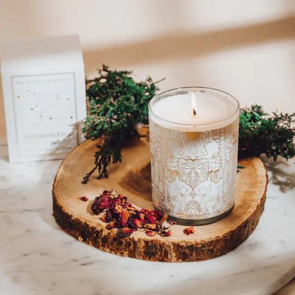 Lit candle in a glass jar on a wood slice with dried petals