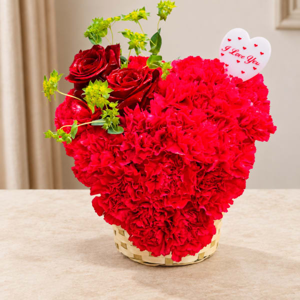 Red carnations and roses in a woven basket with a heart card
