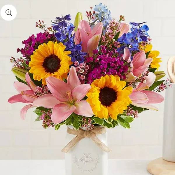Bouquet of sunflowers, pink lilies, and blue flowers in a white vase