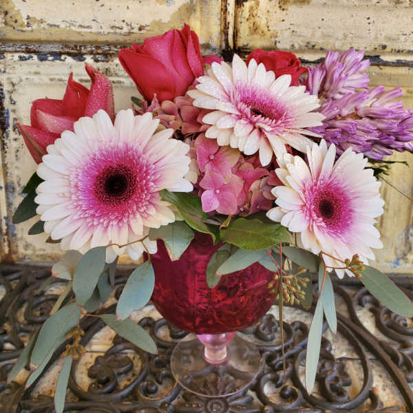 Pink and white gerbera daisies with roses in a red glass vase