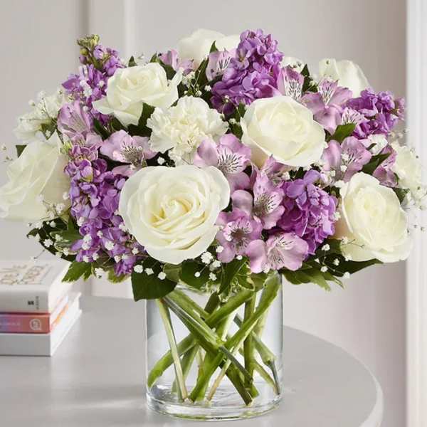 Bouquet of white roses and purple flowers in a clear glass vase