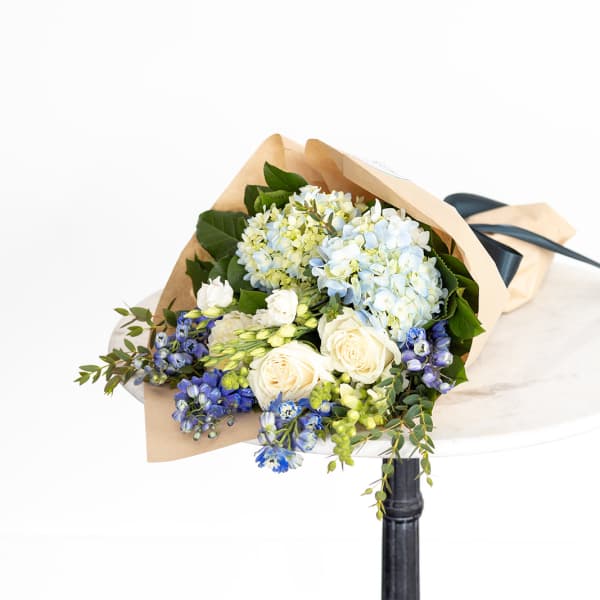 Bouquet of blue hydrangeas, white roses, and blue flowers wrapped in paper