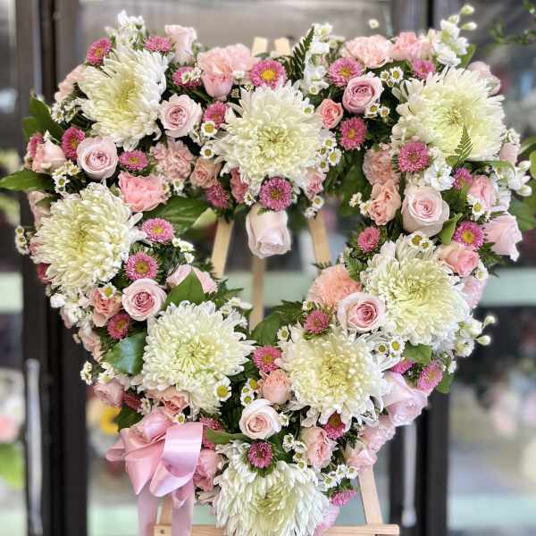 Heart-shaped floral wreath with pink and white flowers on an easel
