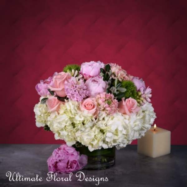 Pink and white floral arrangement in a glass vase beside a lit candle
