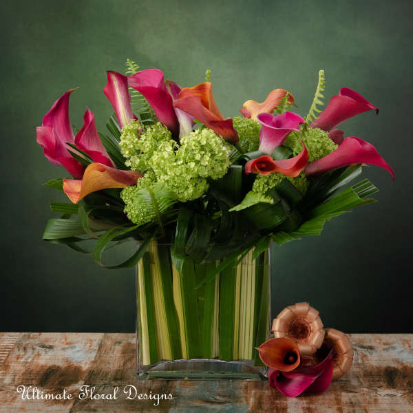Modern arrangement of pink and orange calla lilies with green blooms in a leaf-lined glass cube vase