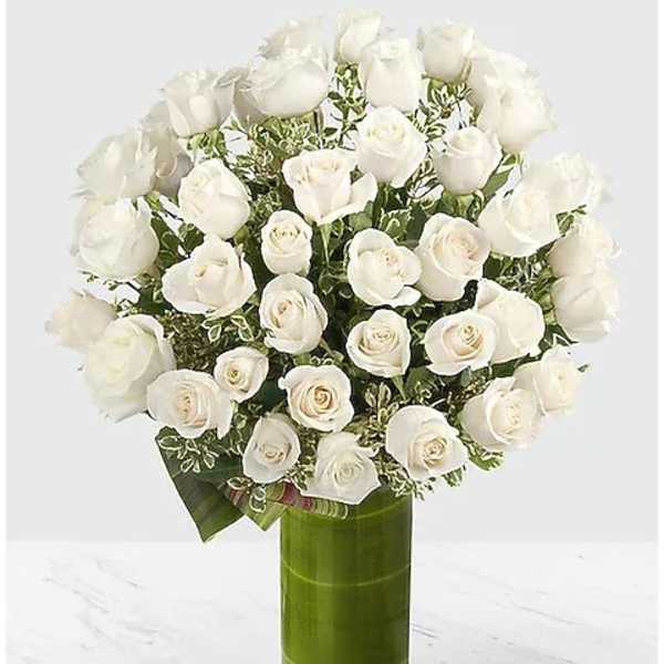White roses arranged in a tall green glass vase