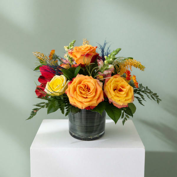 Colorful rose arrangement in a glass vase on a white pedestal