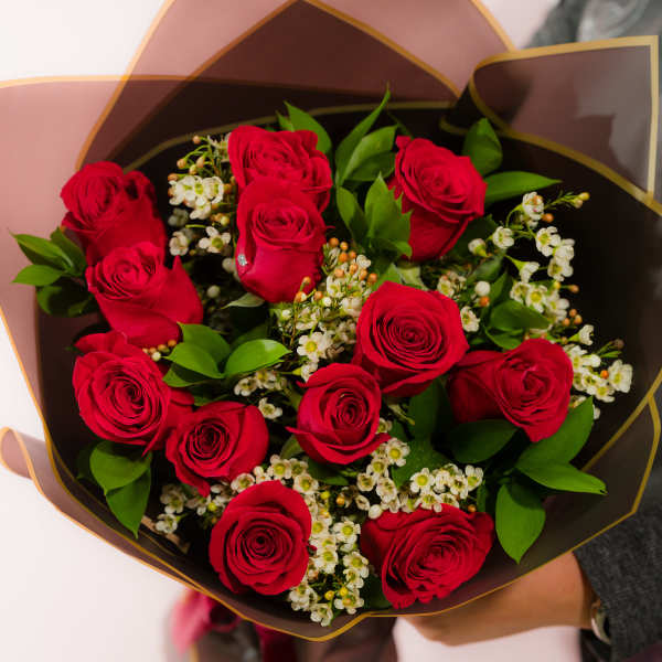 Bouquet of red roses with white filler flowers in dark wrapping