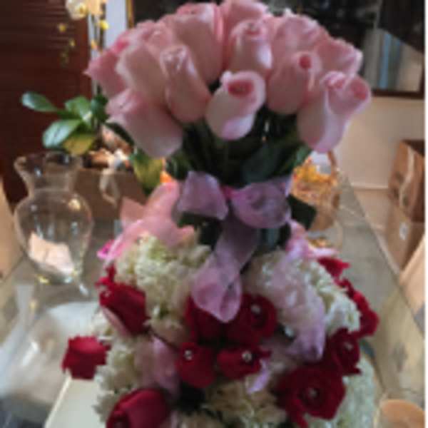 Tall arrangement of pink roses above a dome of white blooms with red roses and pink ribbon
