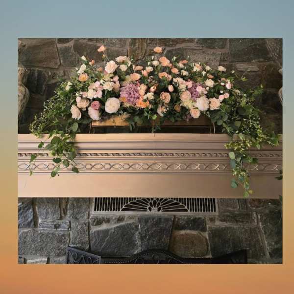 Large pastel floral arrangement with roses and hydrangeas on a mantel