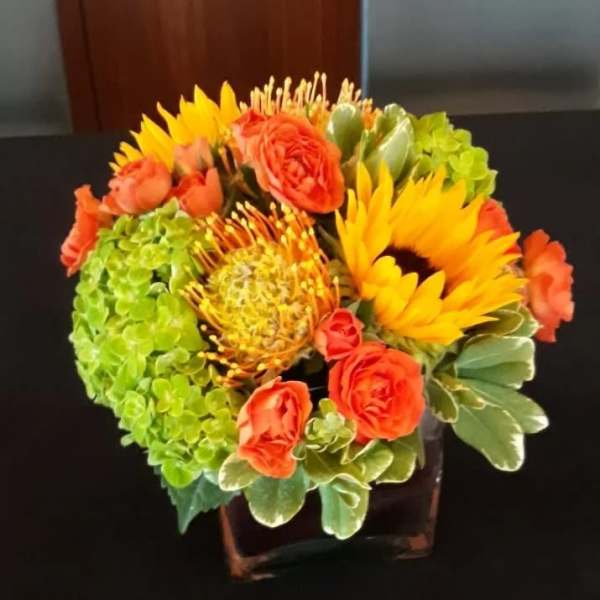 Orange roses and yellow sunflowers in a square vase