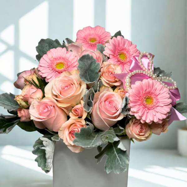 Pink roses and gerbera daisies in a white vase with a ribbon bow