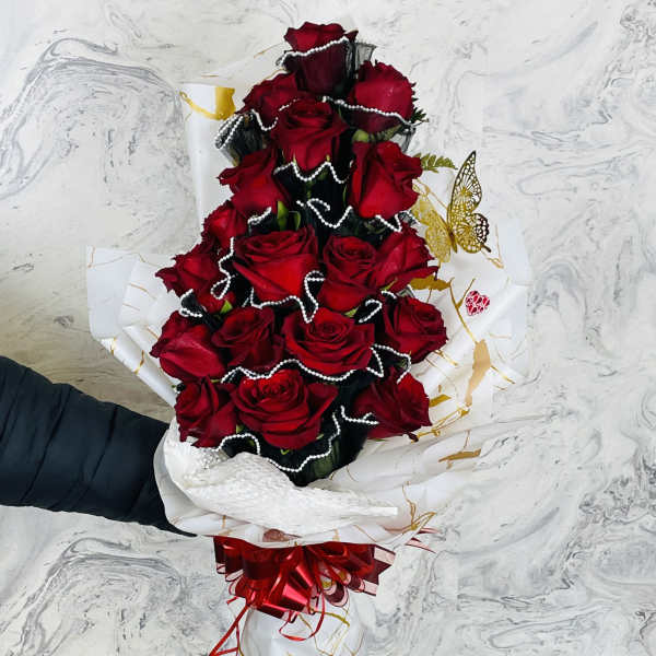 Tall bouquet of red roses wrapped in white paper with a red bow