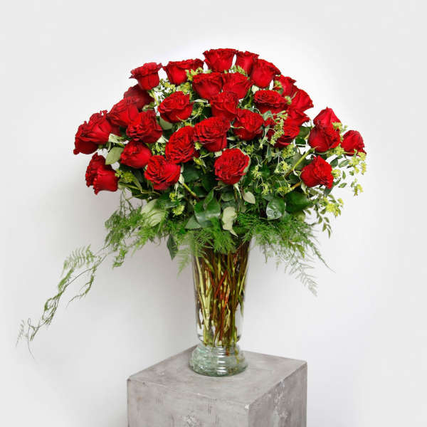 Tall vase arrangement of red roses with greenery