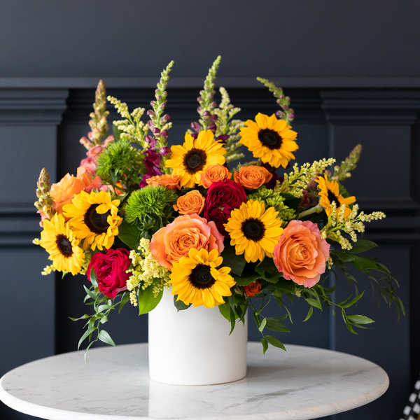Bright mixed bouquet in a white vase with sunflowers and roses