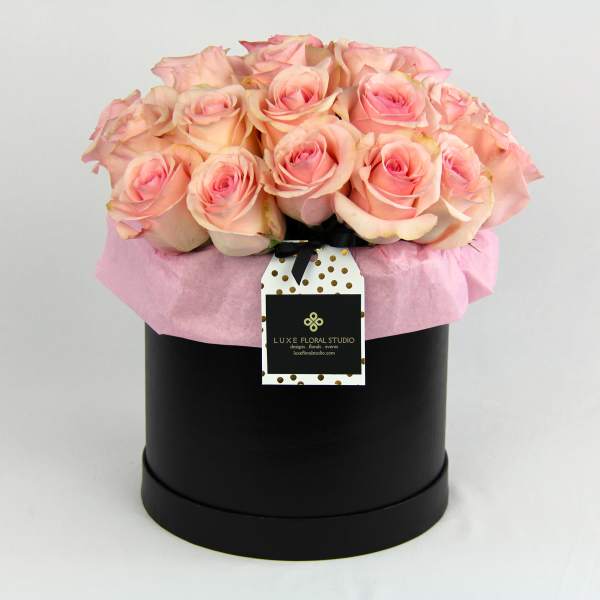 Pink roses arranged in a black hat box with a hanging tag