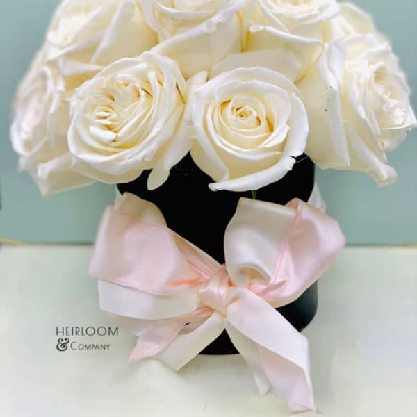 White roses arranged in a black vase with a pale pink ribbon