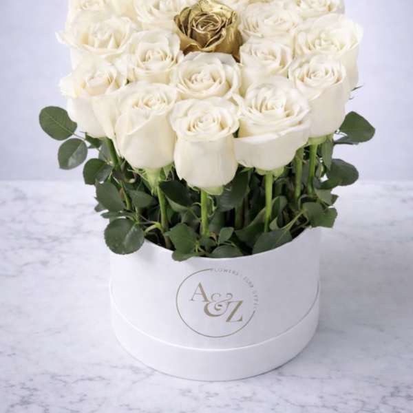 White roses arranged in a round white box with a gold rose at center