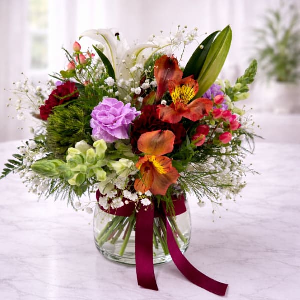 Mixed bouquet in a clear glass vase with a burgundy ribbon