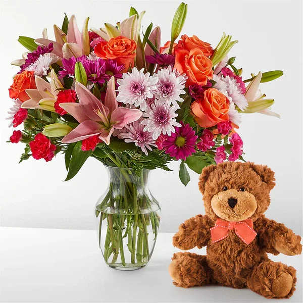 Mixed bouquet in a glass vase beside a teddy bear