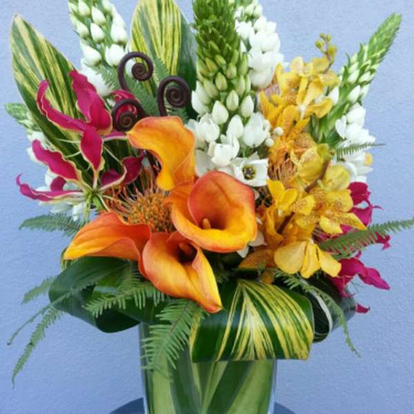 Tropical bouquet with orange calla lilies and yellow orchids in a glass vase