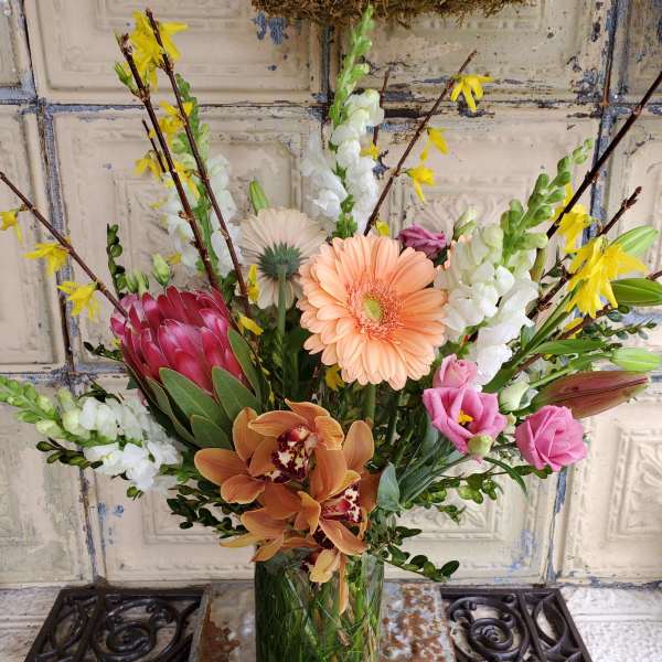 Mixed bouquet in a clear glass vase with pink, peach, white, and yellow blooms
