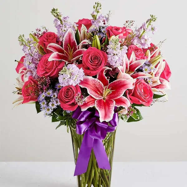 Bouquet of pink roses and lilies in a clear glass vase with a purple ribbon