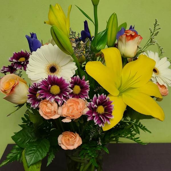 Mixed bouquet with yellow lilies, white gerberas, and peach roses in a glass vase