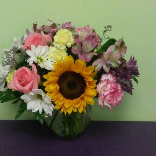 Mixed bouquet with a sunflower, pink roses, and white daisies in a glass vase