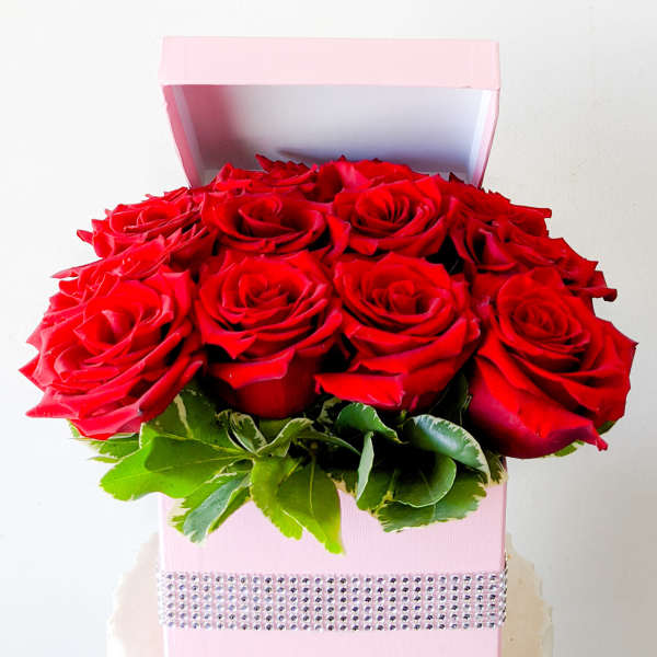 Red roses arranged in a pink gift box with a rhinestone band